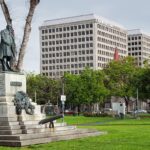 a statue of a man in a park with a cannon in front of buildings